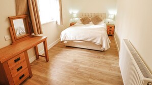 Ein Schlafzimmer mit einem hölzernen Bett, Nachttischen, einem kleinen Tischchen, einem Spiegel und einer Heizung.