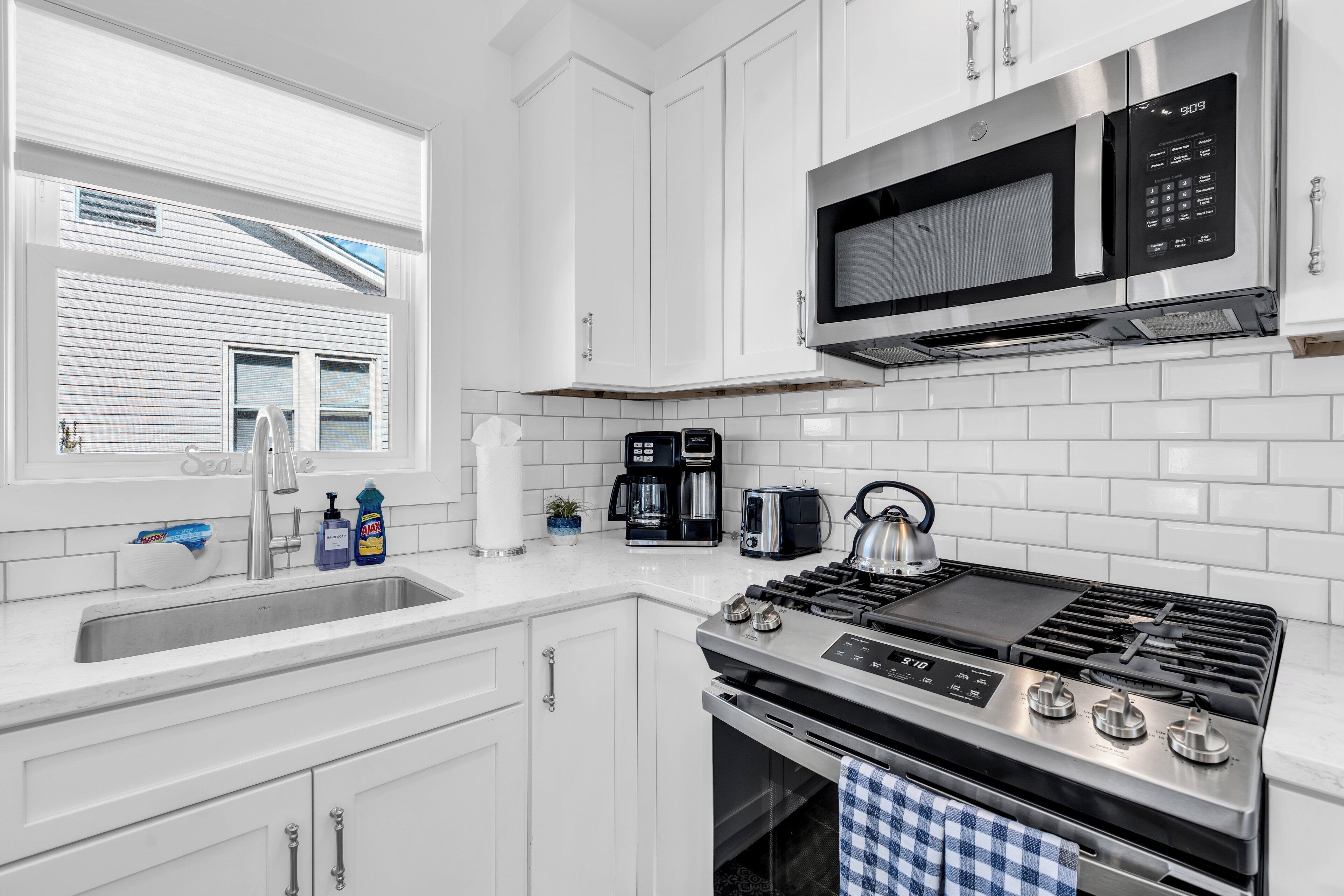 A modern kitchen with white cabinetry, a stainless steel stove, a microwave, and a coffee maker.