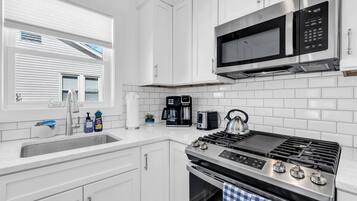 A modern kitchen with white cabinetry, a stainless steel stove, a microwave, and a coffee maker.