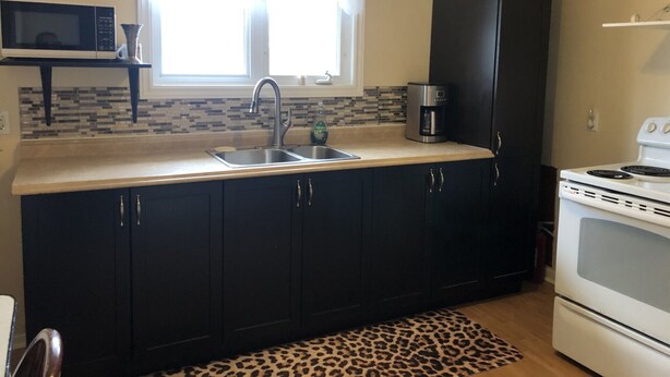 A kitchen with dark cabinets, a stainless steel sink, a microwave, a coffee maker, and a stove. - Downtown walkable to restaurants, bars public transportation and the waterfront. (Charlottetown)