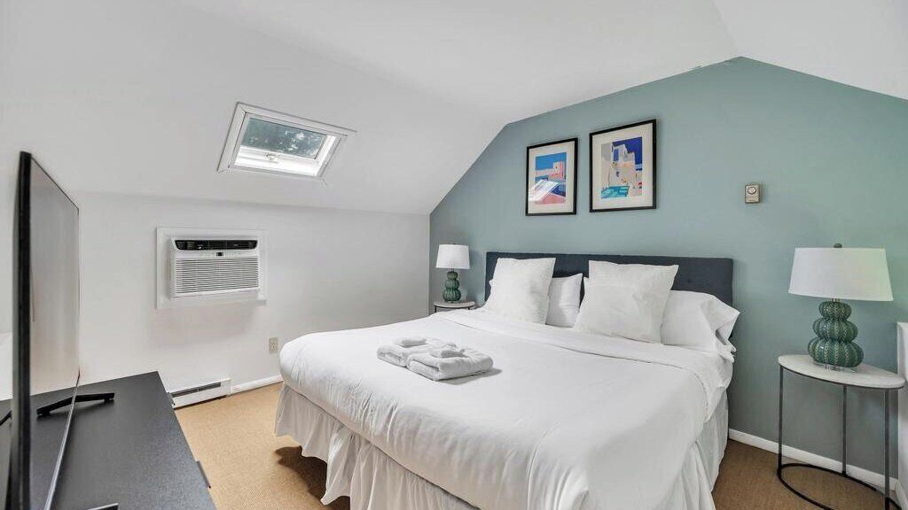 Ein Schlafzimmer mit einem Bett, zwei Nachttischen, einem Fenster mit Klimaanlage und einem Deckenventilator.