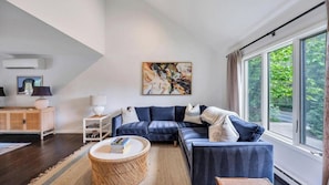 A modern living room with a sectional sofa, a coffee table, a side table, and a large window with a view of greenery.
