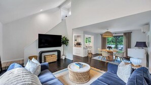 A modern living room with a sofa set, a flat-screen TV, a fireplace, and a dining area with a table and chairs. - Modern Sag Harbor Escape, Moments from the Water and Long Beach to View... (Sag Harbor)