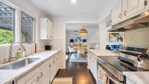 A modern kitchen with a large window, white cabinetry, a built-in oven, and a dining area with a table and chairs. - Modern Sag Harbor Escape, Moments from the Water and Long Beach to View... (Sag Harbor)