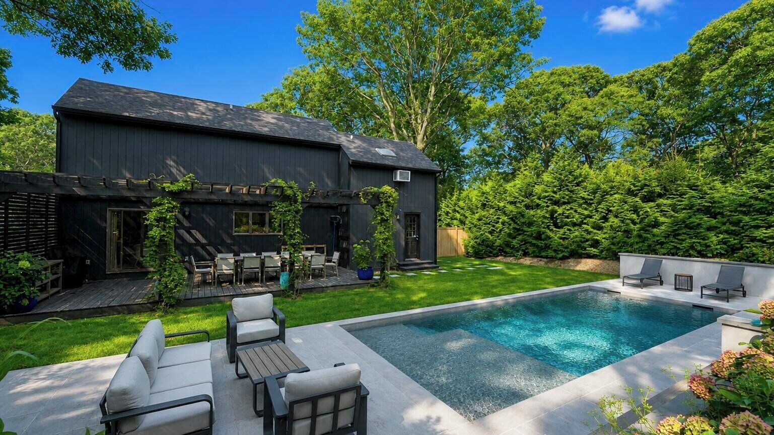 Una casa moderna con piscina, mobiliario de exterior y un jardín cuidado.