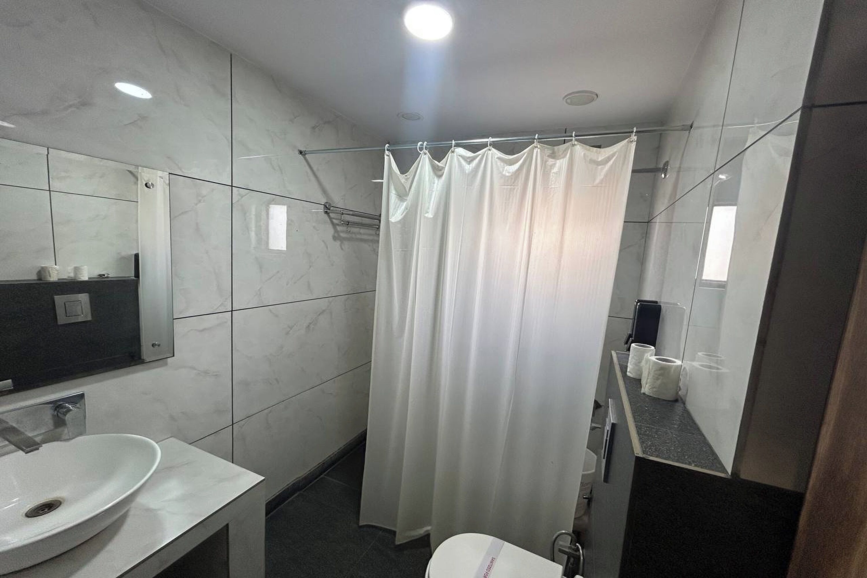 A modern bathroom with a white sink, a mirror, a shower curtain, and a toilet.