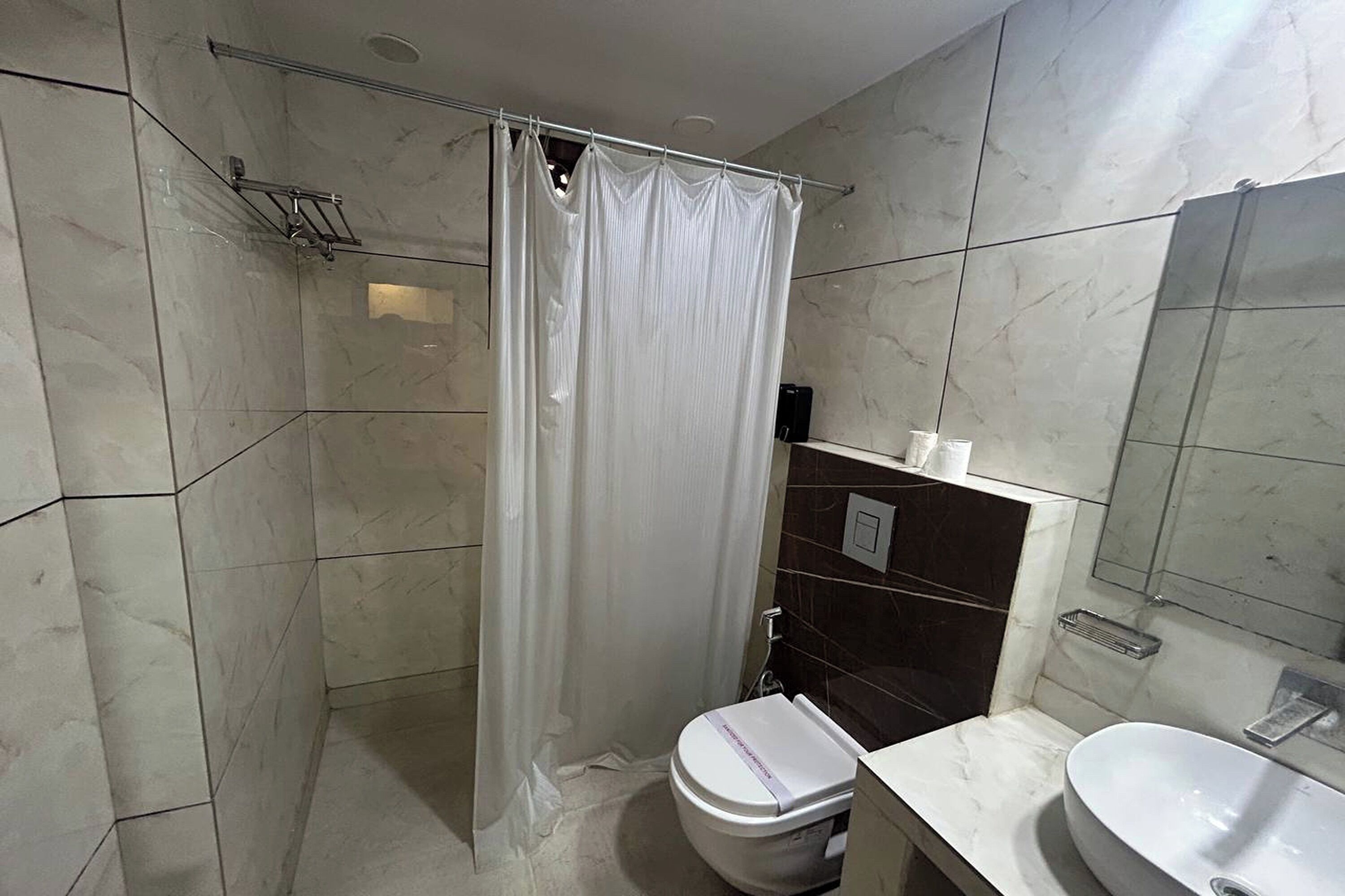 Une salle de bain avec un rideau de douche, des toilettes, un lavabo et un miroir.