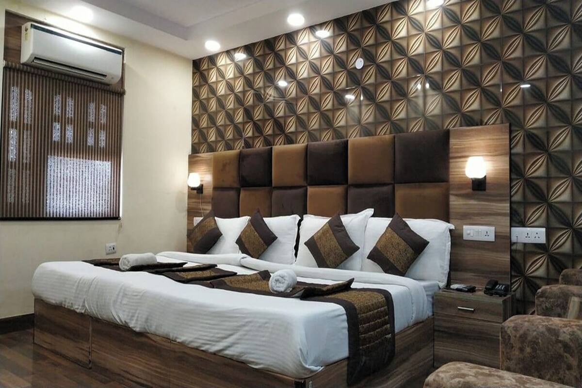 Habitación de hotel con una cama grande, cabecera con diseño geométrico, mesita de noche con lámpara y aire acondicionado de pared.