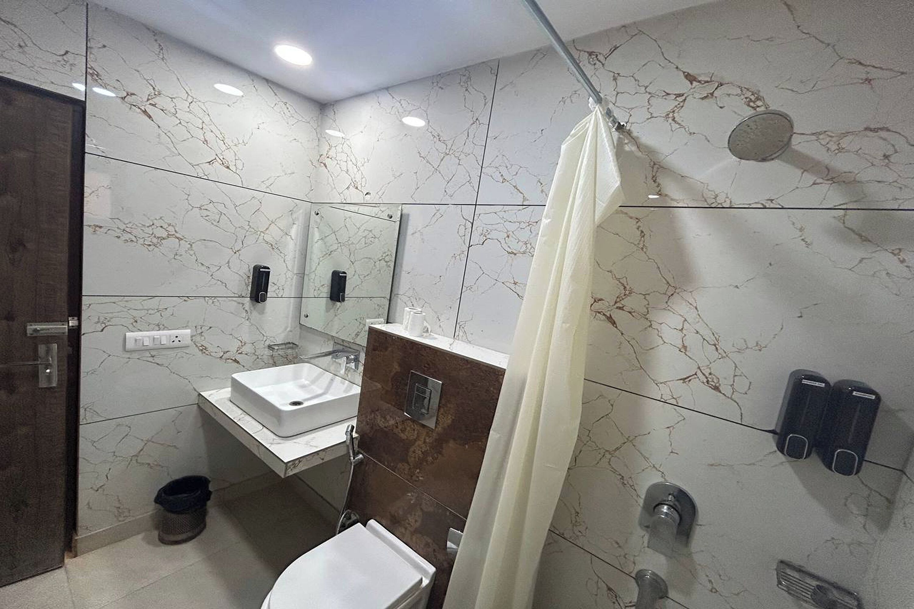 Ein modernes Badezimmer mit Marmorfliesenspiegel, einem weißen Waschbecken, einer Duschkabine mit Vorhang und einer Toilette.