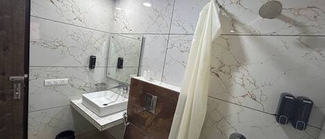 Ein modernes Badezimmer mit Marmorfliesenspiegel, einem weißen Waschbecken, einer Duschkabine mit Vorhang und einer Toilette.