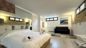 Een hotelkamer met een groot bed, een zwarte bank, een houten vloer, een stenen muur en een schilderij van een kustlandschap.