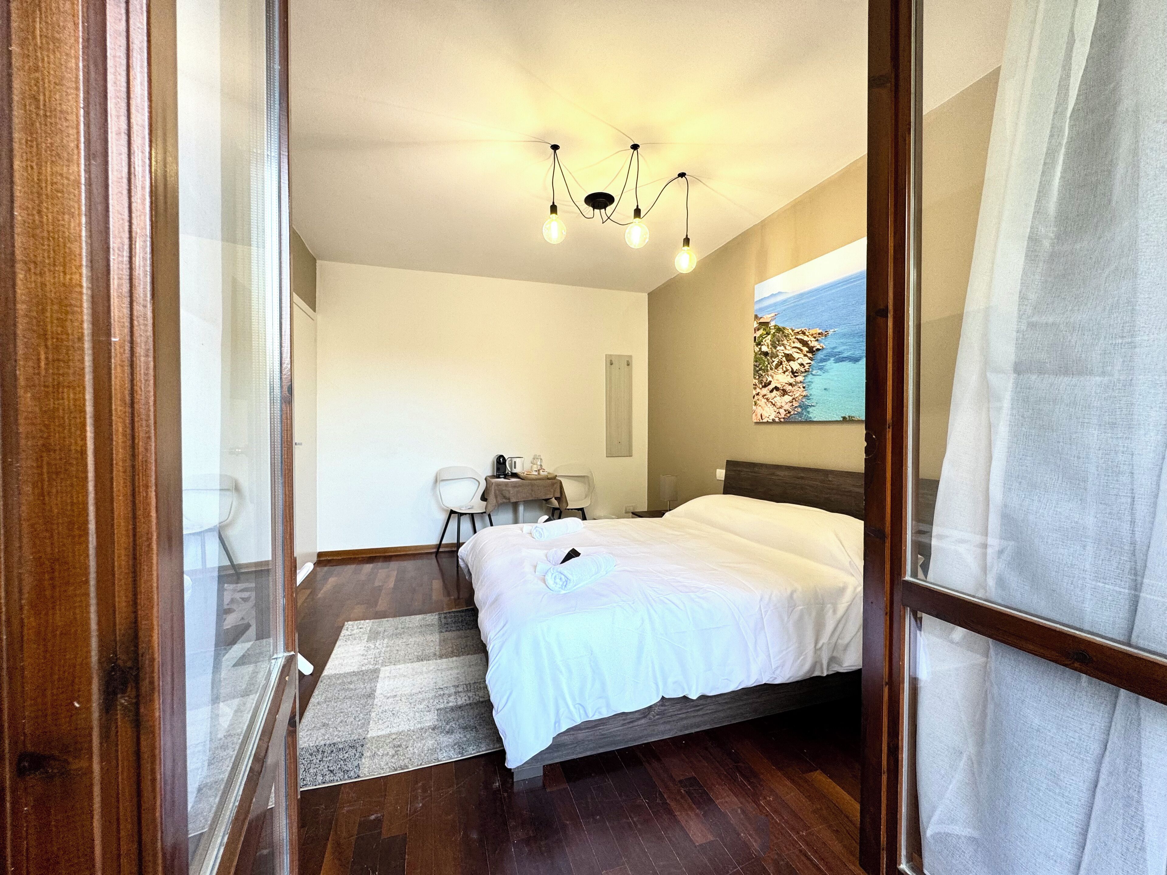 A bedroom with a bed, a desk, a chair, a rug, and a painting on the wall.