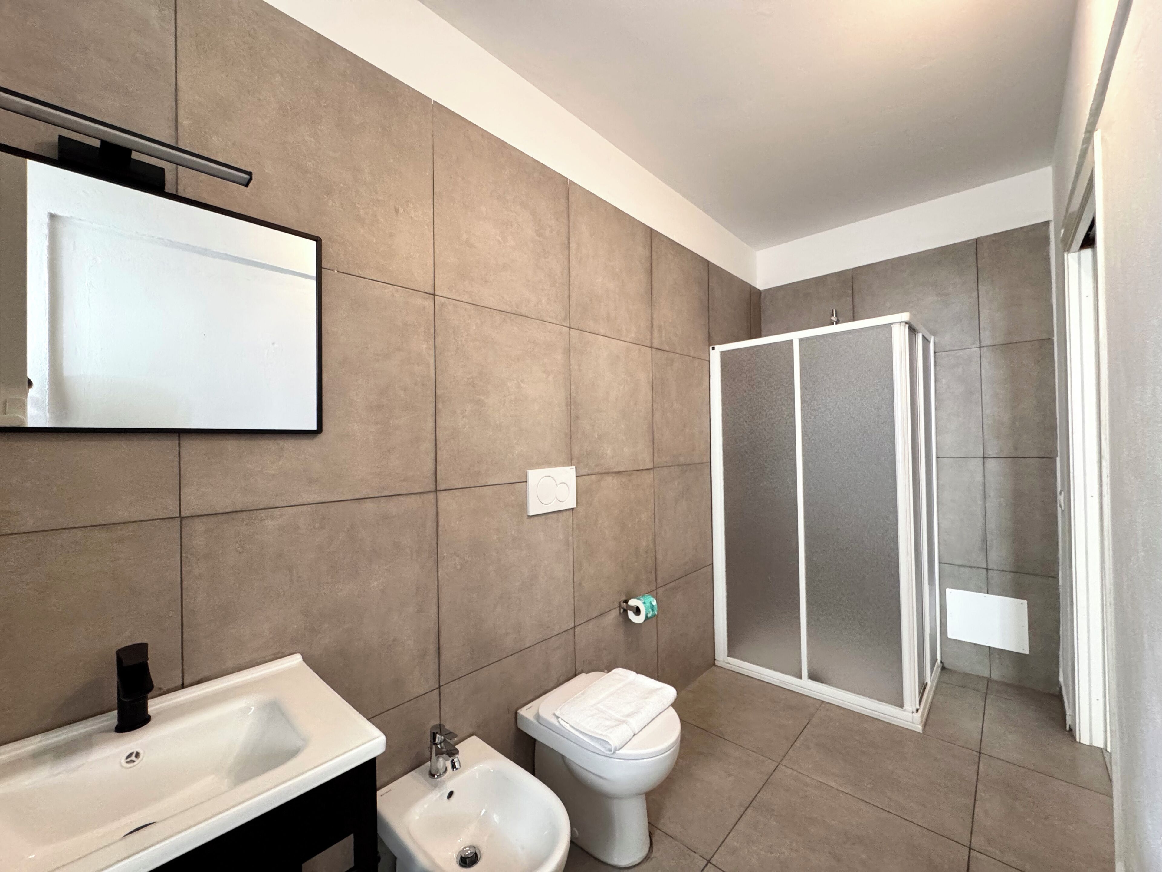 A modern bathroom with a sink, bidet, toilet, and a glass shower enclosure.