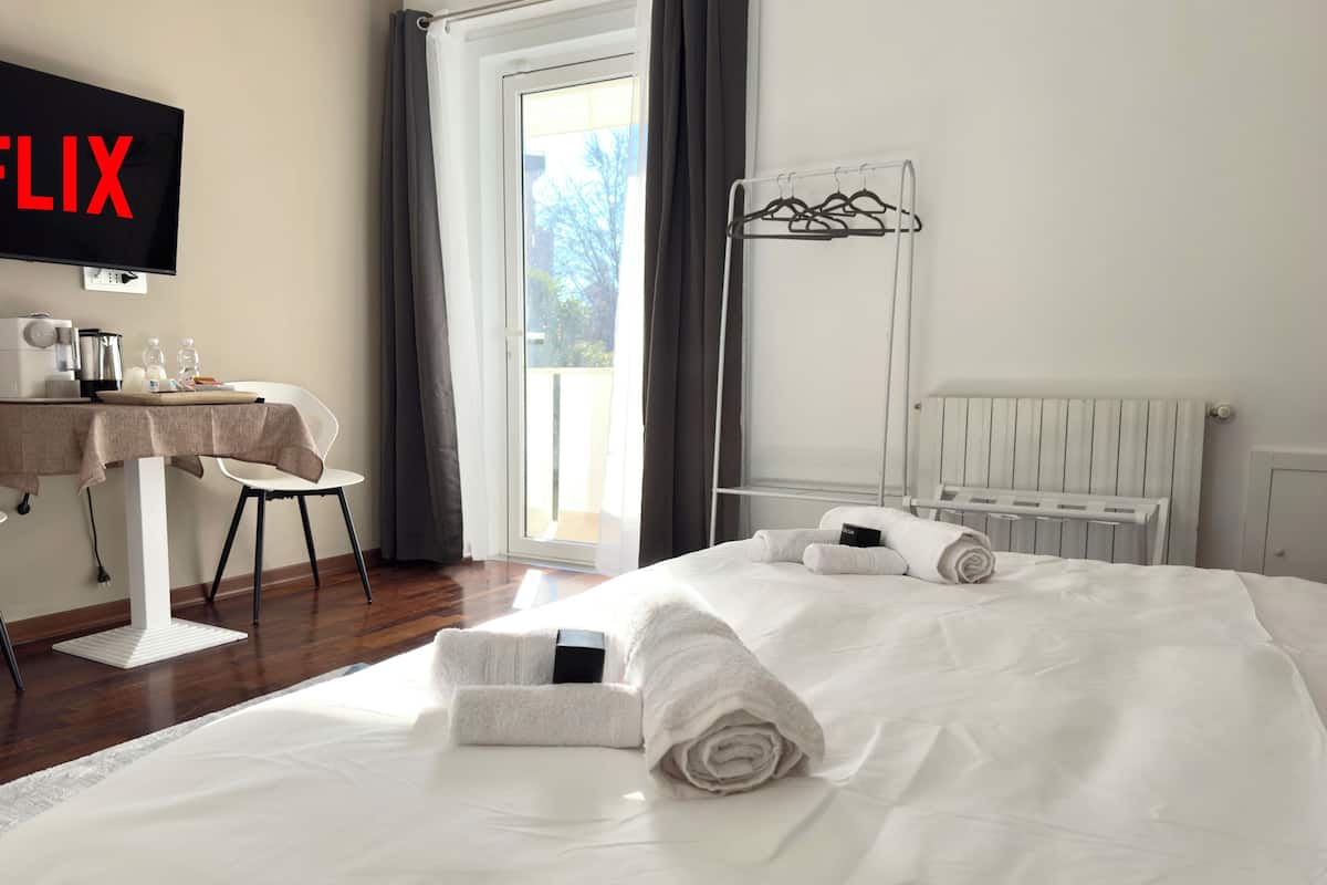 Une chambre d’hôtel avec un lit, un bureau et une chaise, une télévision et une fenêtre avec des rideaux.