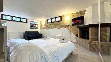 A bedroom with a large bed, a black sofa, a stone wall, a fireplace, and a TV displaying 'NETFLIX'.