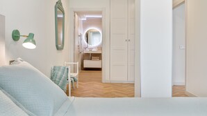 Un dormitorio con cama, mesita de noche, espejo y lámpara de pared.