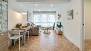 Una sala de estar moderna con comedor, ventanas grandes y piso de madera en espiga.