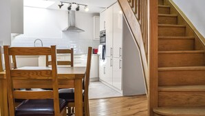 Een moderne keuken met witte kasten, een eettafel met houten stoelen en een trap met houten leuningen.