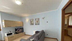 Ett modernt vardagsrum med en grå soffa, träskåp, en platt-TV och konstverk på väggen.