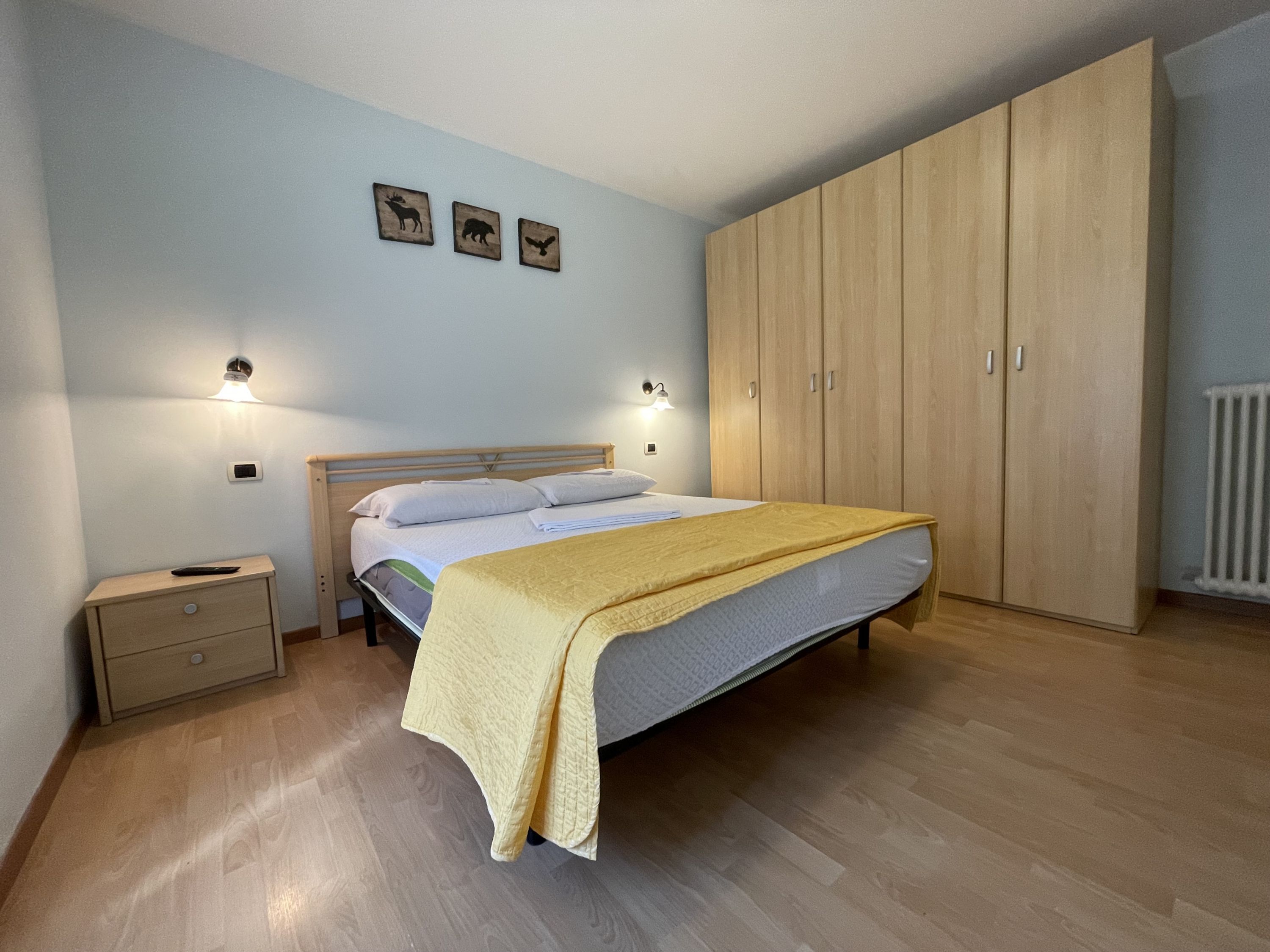 Une chambre à coucher comprenant un lit, des tables de chevet, une armoire et des lampes fixées au mur.