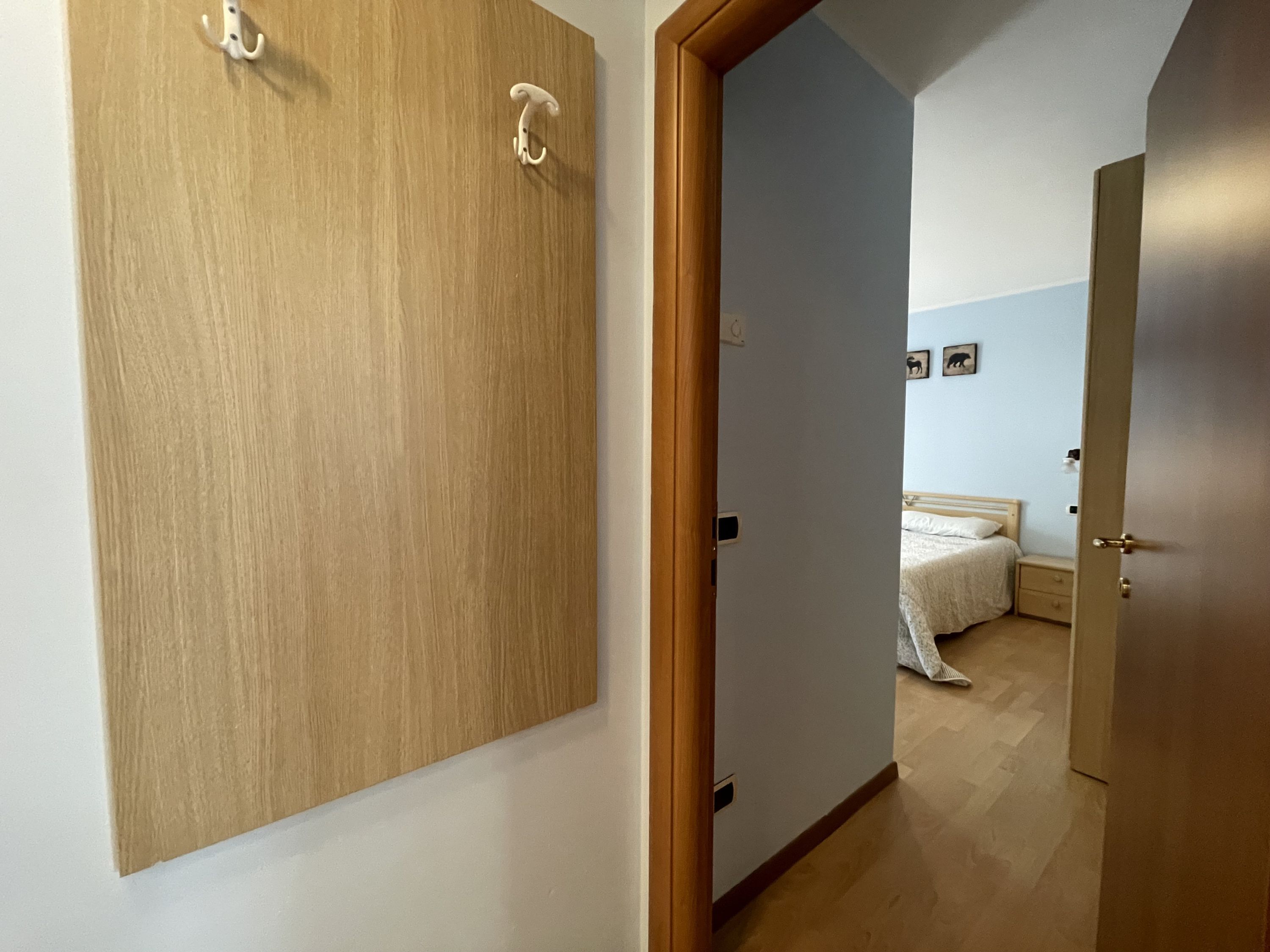 Un couloir avec des portes en bois, un lit recouvert d’une courtepointe blanche et une petite table de chevet.
