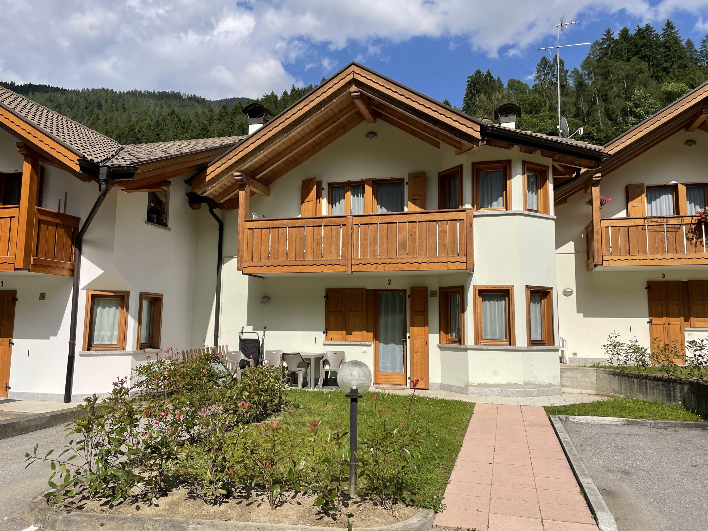 Un chalet a due piani con balconi in legno, un vialetto lastricato e un'area giardino.