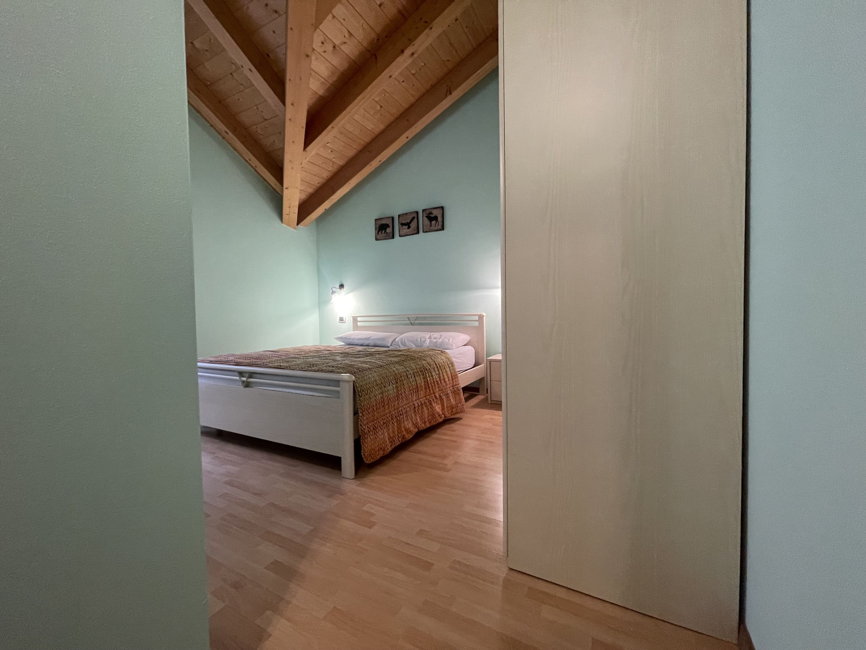 A bedroom with a wooden ceiling, a bed with a patterned blanket, and a nightstand with a lamp.