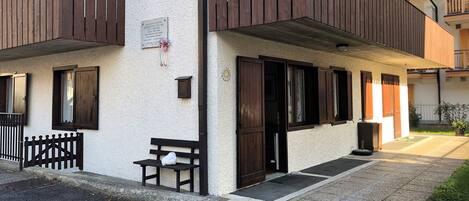 A building with a white exterior, wooden balconies, and a bench outside.