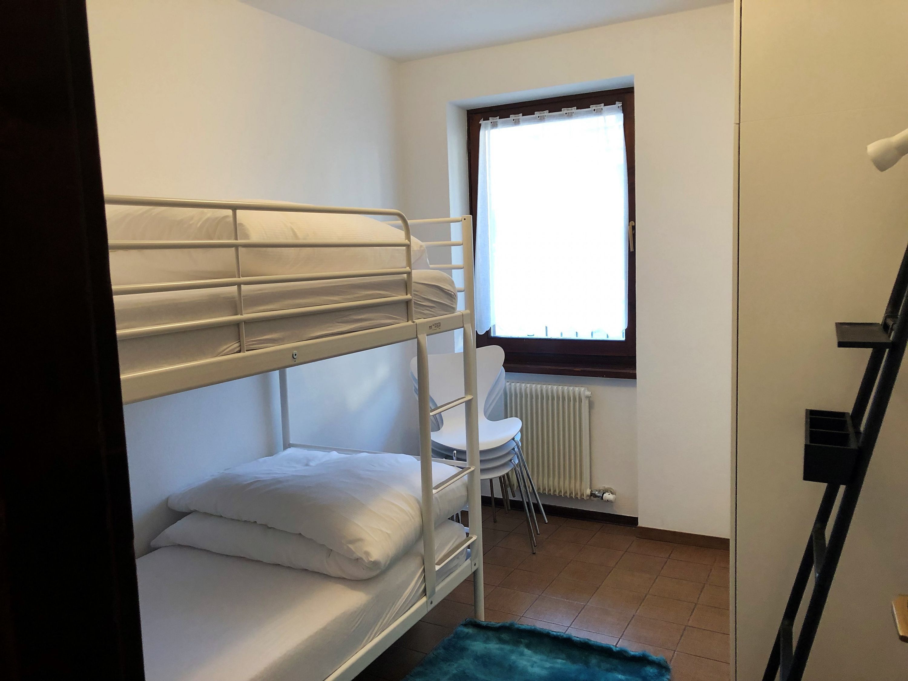 A bunk bed room with a window, radiator, and a chair.