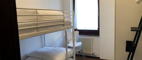 A bunk bed room with a window, radiator, and a chair.