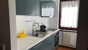 Una cocina compacta con un lavamanos, un hervidor y una ventana con cortinas.