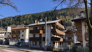 Un edificio de varios pisos con balcones, una señal de paso para peatones y montañas al fondo.