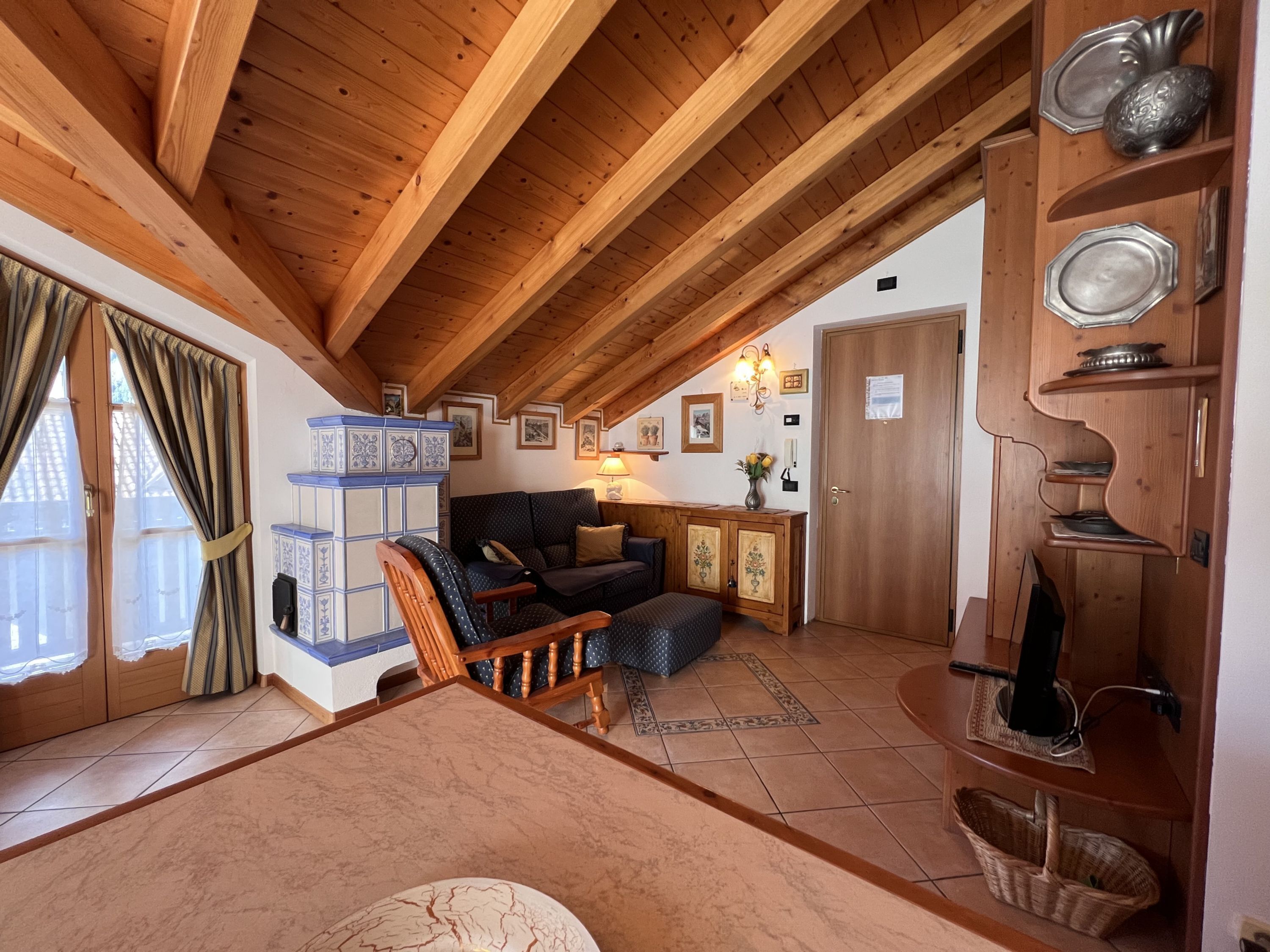 A cozy living room with a wooden ceiling, a sofa, a chair, and a cabinet with decorative plates.