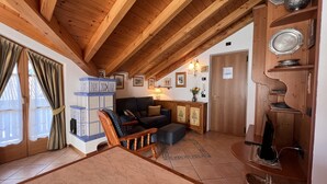 A cozy living room with a wooden ceiling, a sofa, a chair, and a cabinet with decorative plates. - 004 Trilocale di Charme Giustino (Giustino)