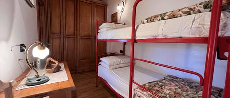 A bunk bed room with wooden flooring, a desk with a lamp, and a wardrobe.
