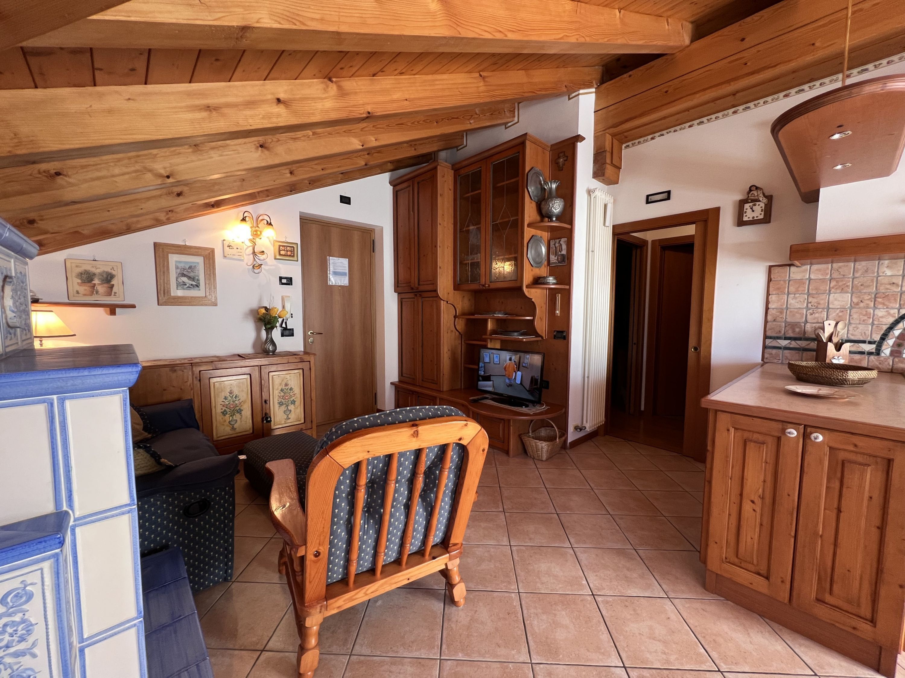 A cozy kitchen with wooden cabinets, a dining area with a blue chair, and a television.