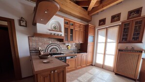 A kitchen with wooden cabinets, a tiled backsplash, and a central island. - 004 Trilocale di Charme Giustino (Giustino)
