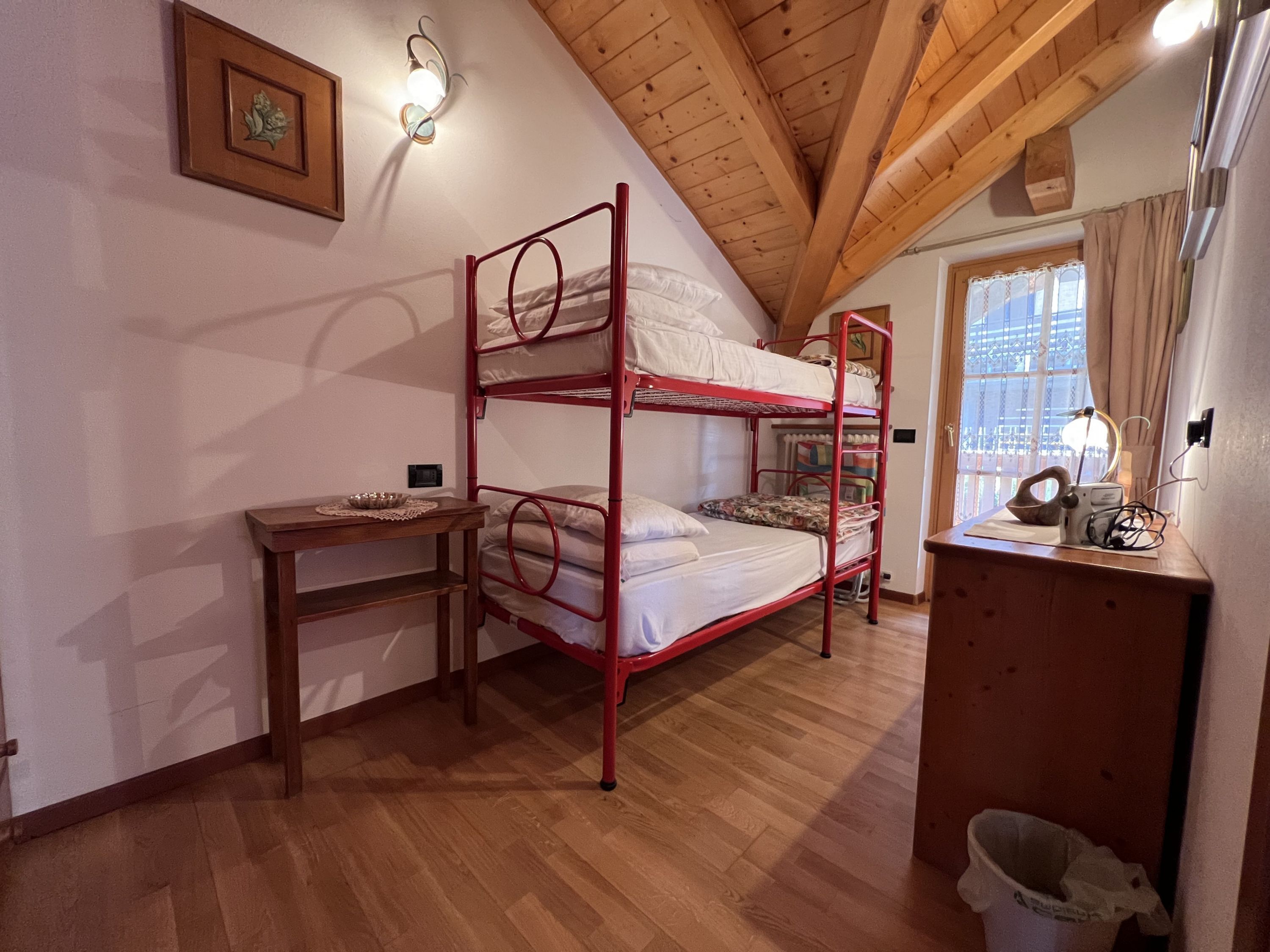 Una camera con letto a castello, una scrivania in legno e un tavolino, un quadro appeso alla parete e una finestra con tende.