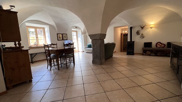 A spacious dining area with a wooden table and chairs, a stone pillar, and a fireplace. - 007 Trilocale con Giardino Giustino (Giustino)