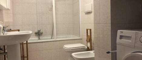 Een moderne badkamer met een wastafel, toilet, bidet en een douchecabine met glazen wanden.