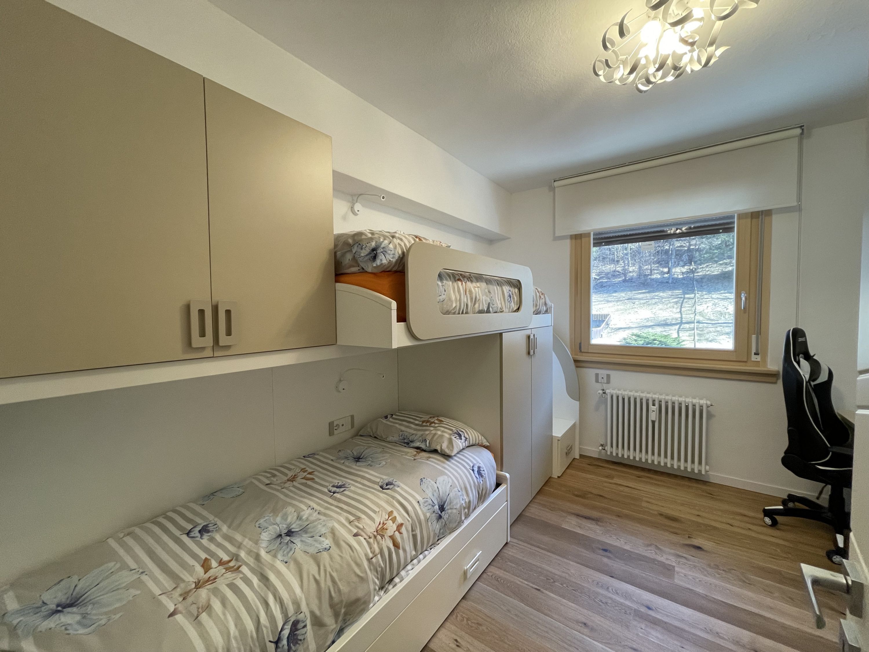 Una camera compatta con un letto a castello, una scrivania e un termosifone.