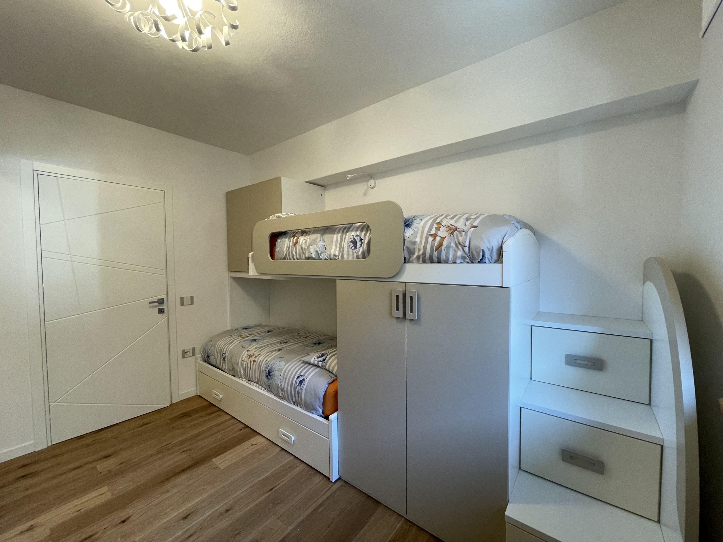 Una habitación pequeña y funcional con una cama nido, un armario y un escritorio.