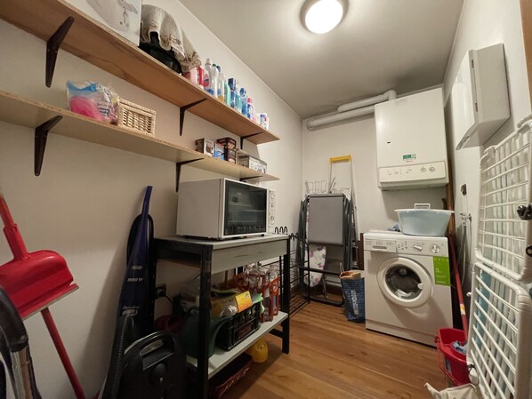 Une buanderie équipée d’un lave-linge, d’un sèche-linge, d’étagères contenant des produits de nettoyage et d’un four à micro-ondes.