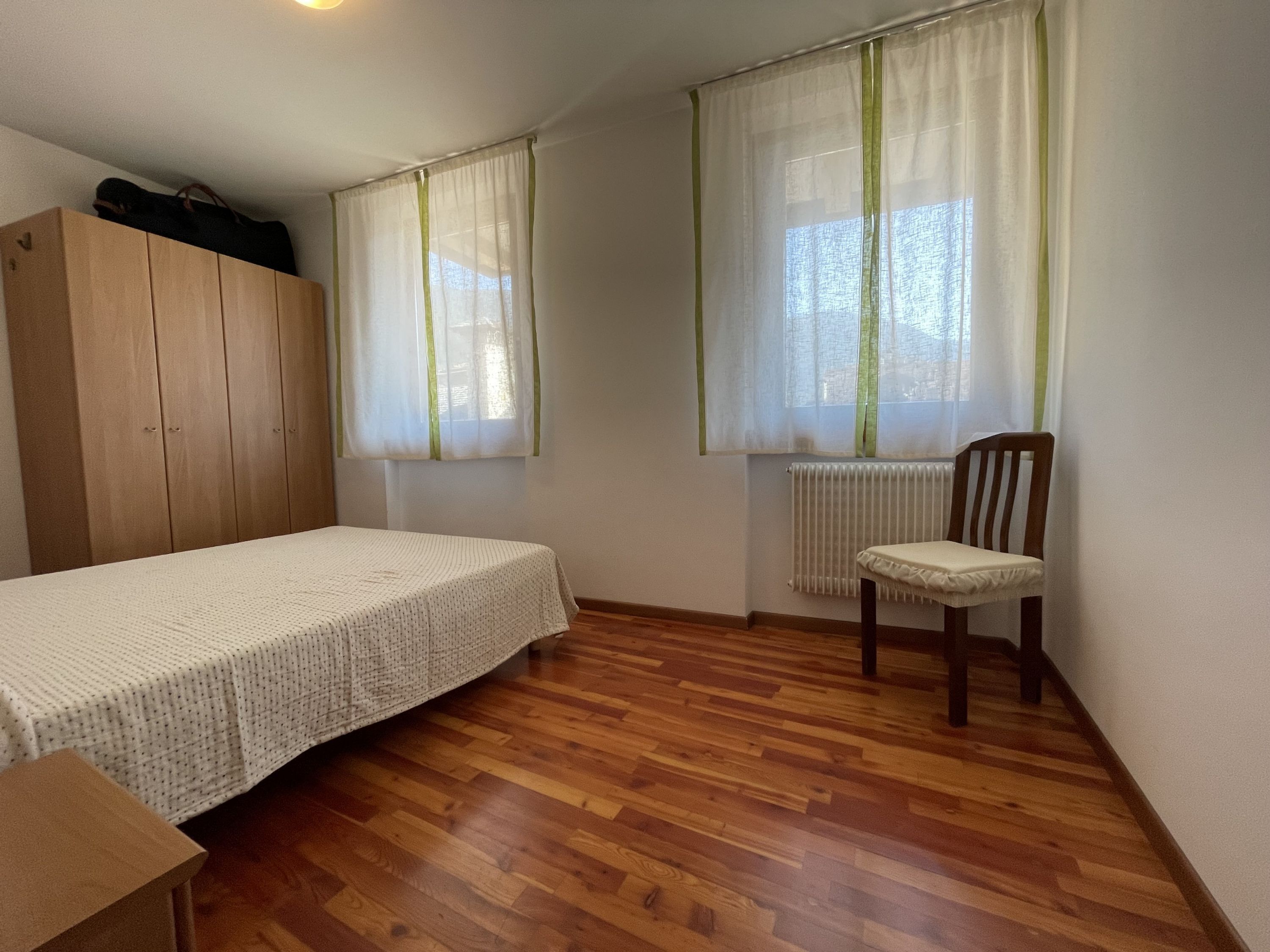 A room with a bed, a chair, a wooden wardrobe, and a radiator.