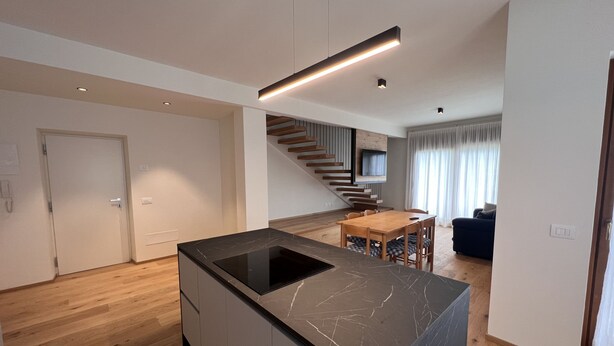 Een moderne keuken met een zwarte marmeren aanrecht, een houten eettafel en een trap die naar een woongedeelte leidt.