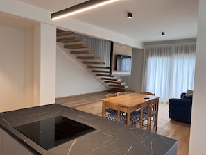 A modern kitchen with a black marble countertop and a built-in stove. There is a wooden dining table with chairs and a blue sofa in the background.