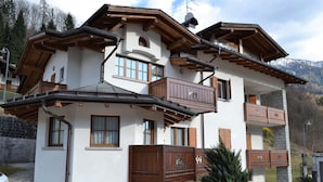 Een chalet met meerdere verdiepingen, houten balkons, stenen trappen en een berg op de achtergrond.