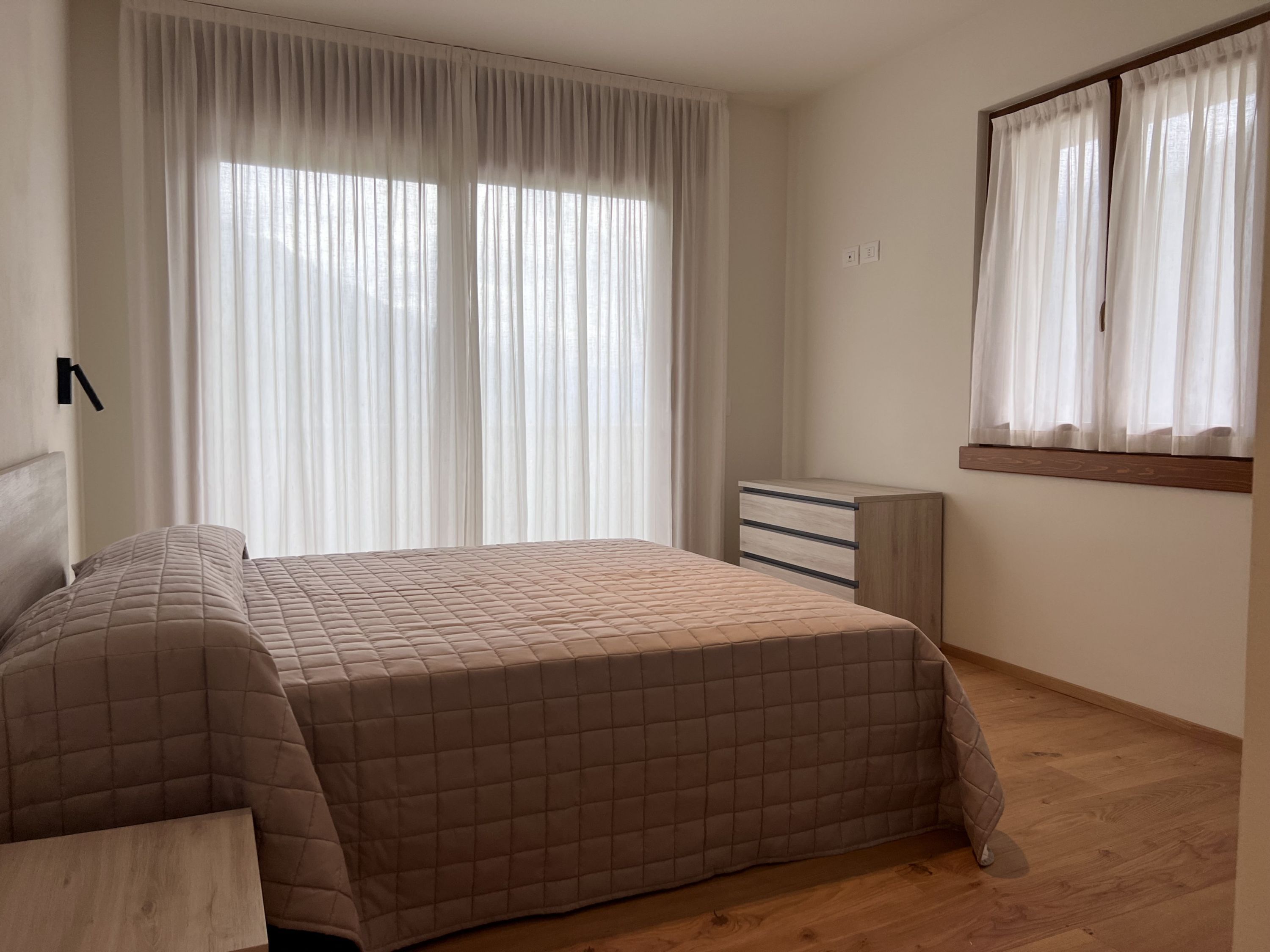 Ein Schlafzimmer mit Bett, Nachttisch, Kommode und einem Fenster mit Vorhängen.