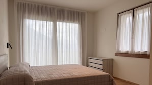Een slaapkamer met een bed, nachtkastje, kaptafel en raam met gordijnen.