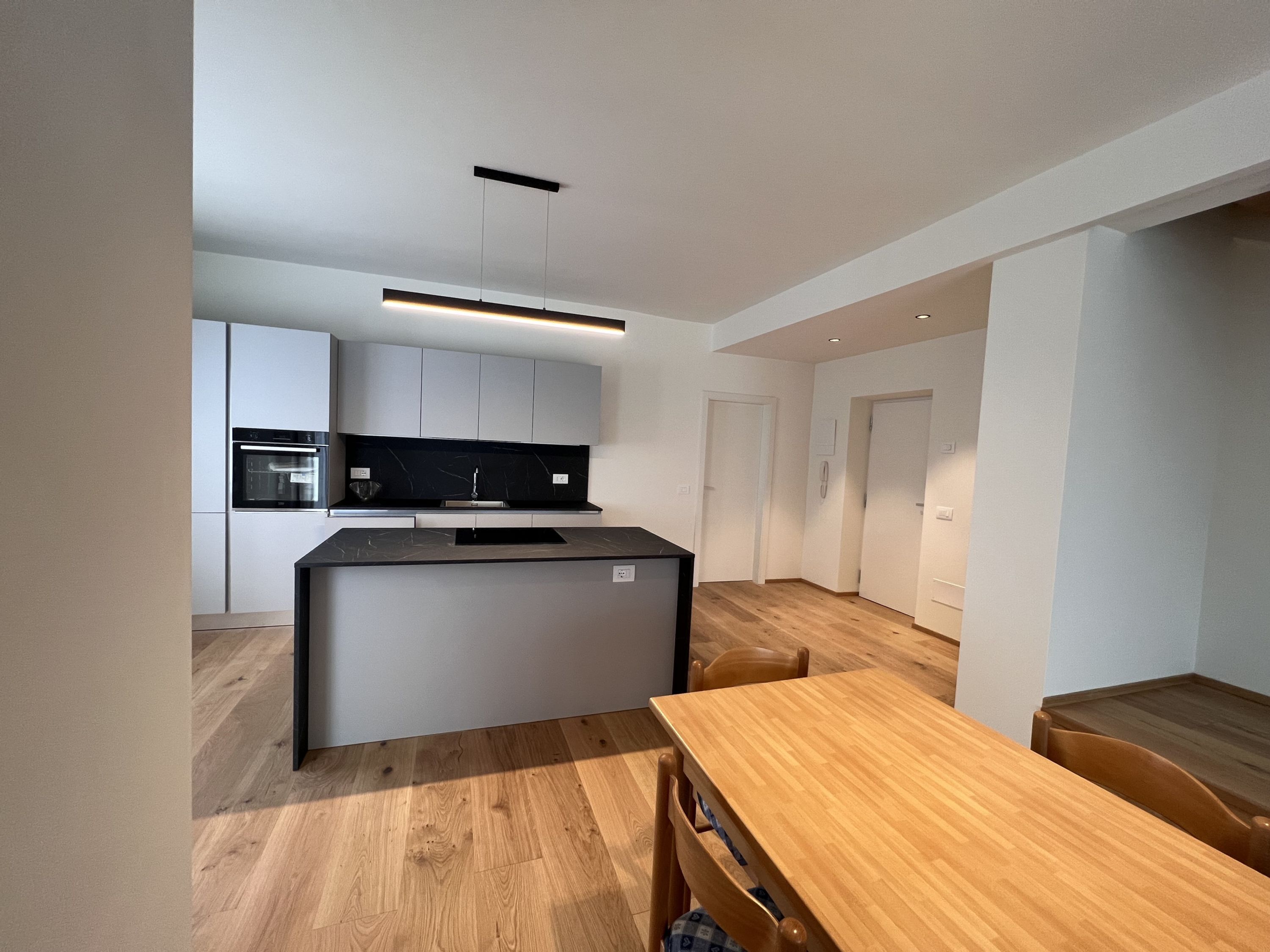 Een moderne keuken met een centraal eiland, inbouwapparatuur en een houten eettafel.